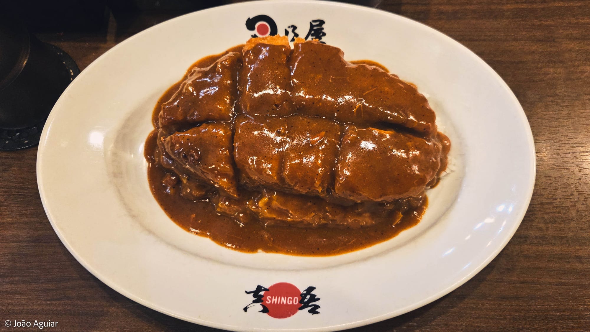 Prato branco largo com um file de porco empanado sobre arroz coberto por molho curry.