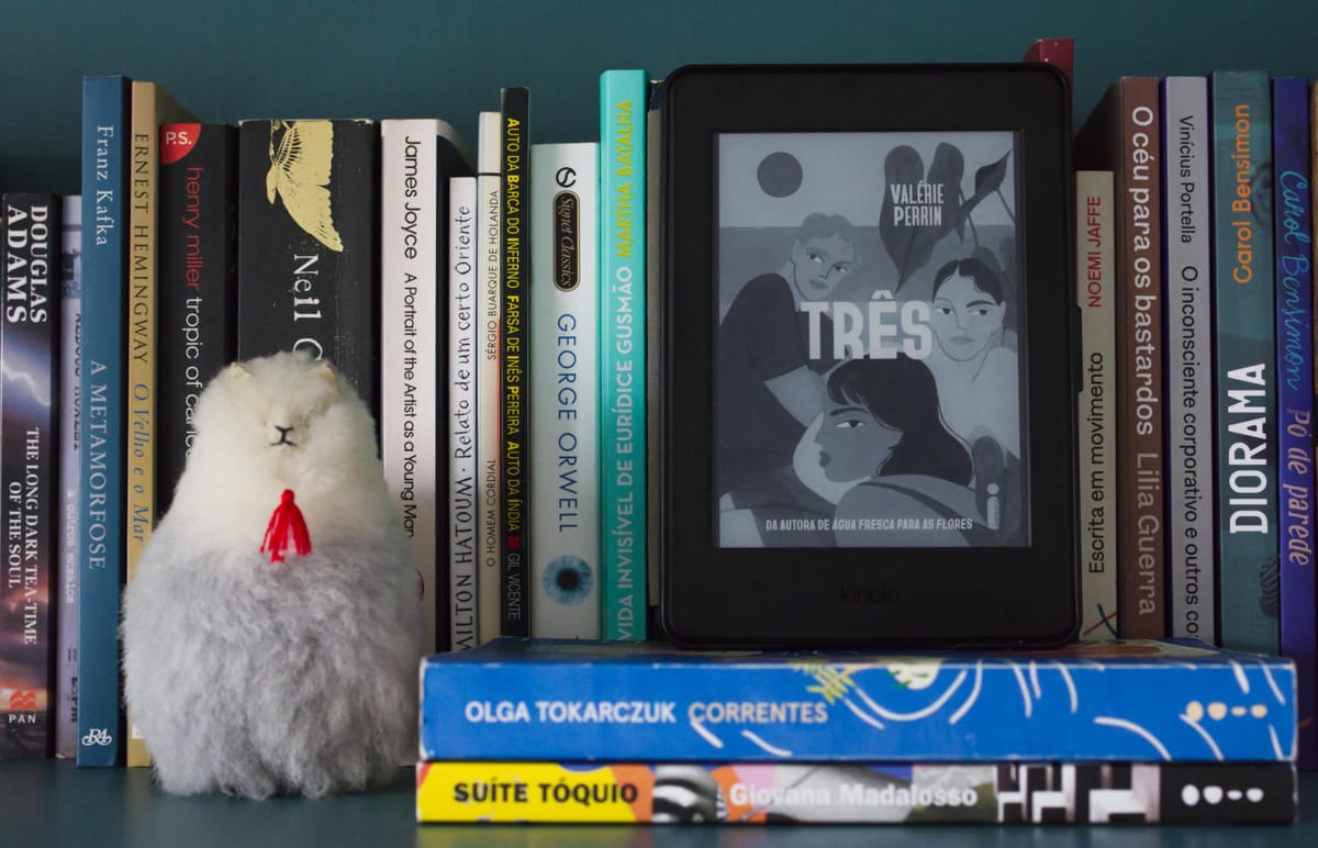 Imagem de um Kindle exibindo a capa do livro "Três" de Valerie Perrin, sobre os livros Correntes, de Olga Tokarczuk e Suite T