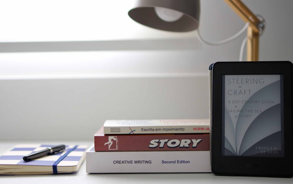 Três livros sobre escrita criativa e storytelling empilhados e um na tela do kindle. Eles são: Story, Creative Writing, Escri