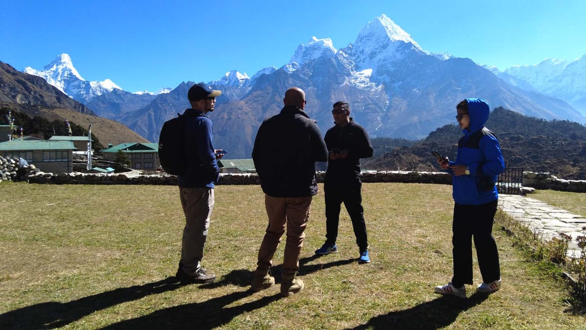 Quatro pessoas conversam de pé sobre um gramado. Elas estão contra a luz, assim que são quase silhuetas. Ao fundo se vê uma g